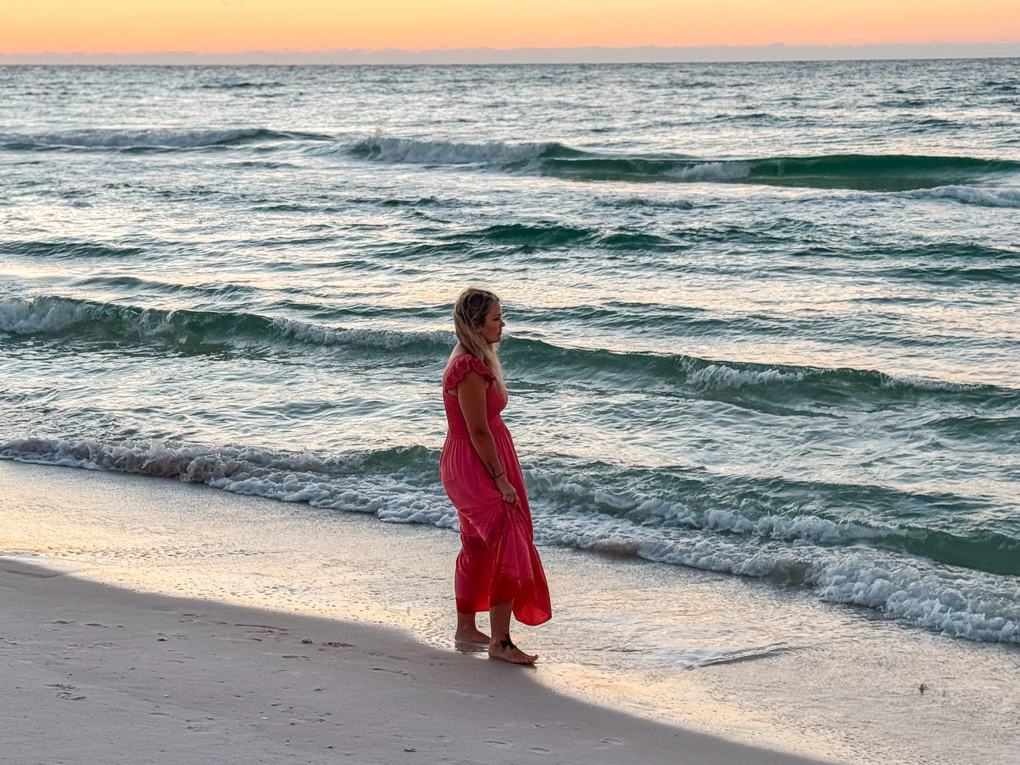 Samantha at sunset on the beach in a pink dress, waves rolling in behind her