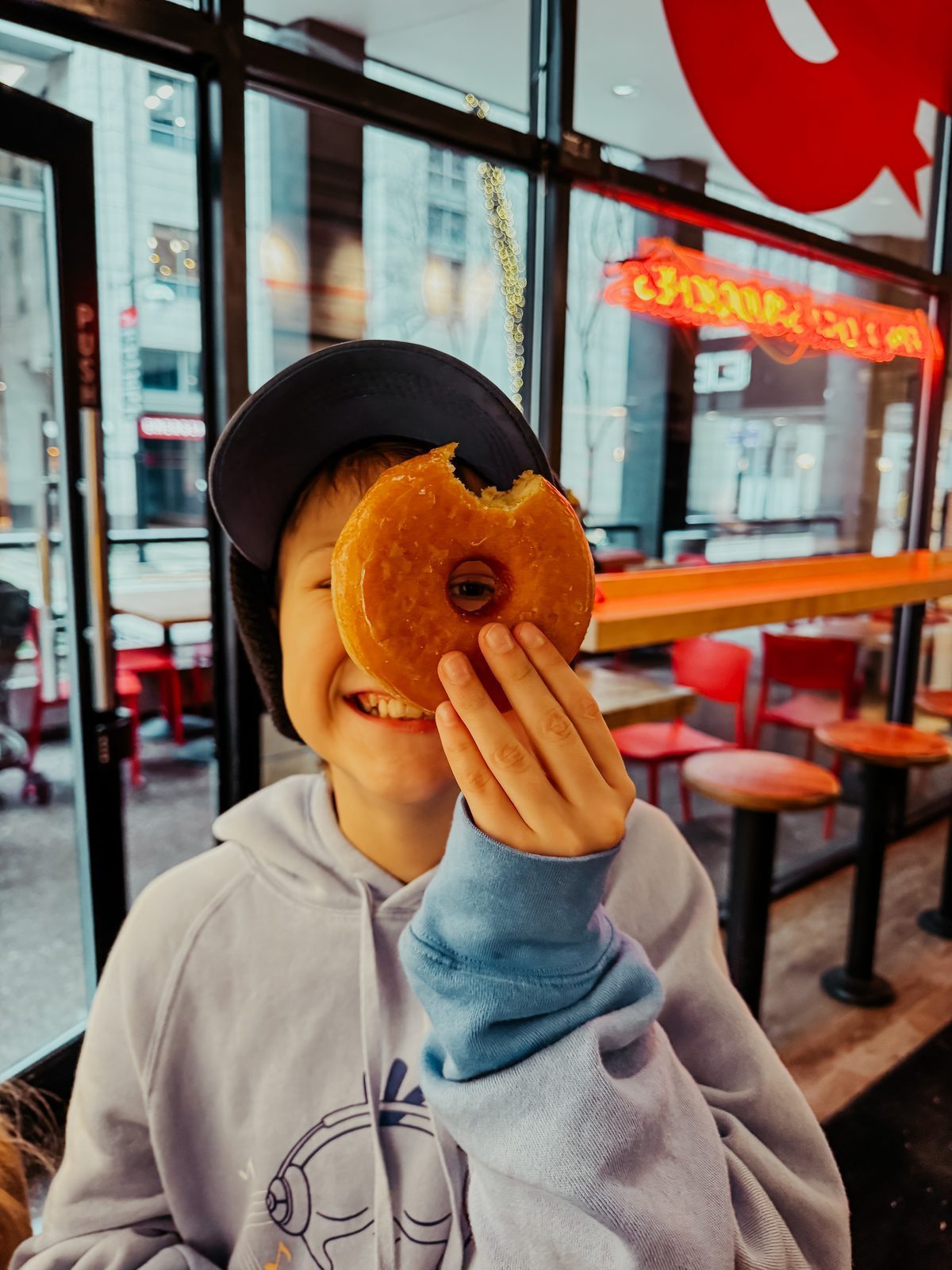 A boy holding a glazed donut over one eye
