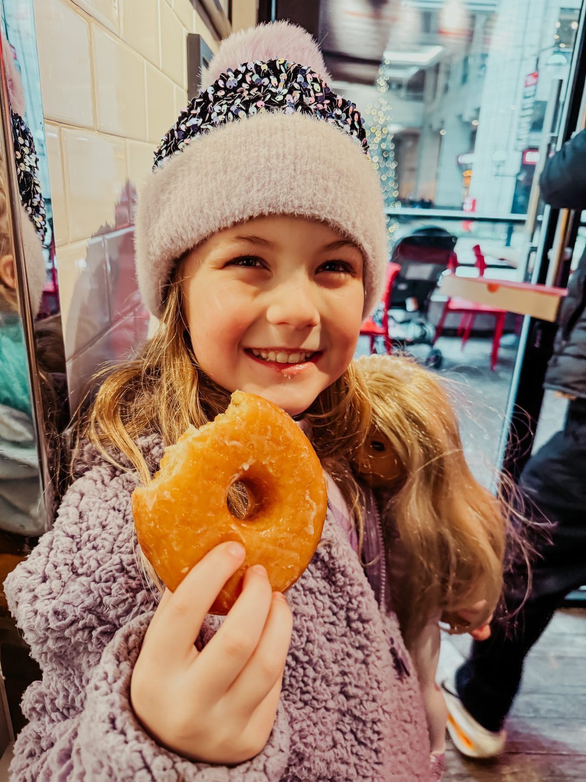 A girl in a pink hat smiling with her donut
