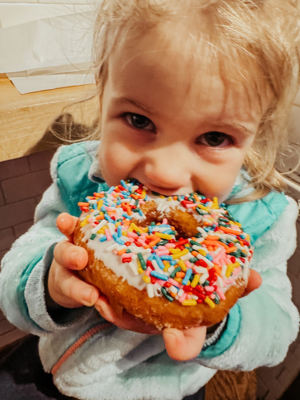 A toddler biting into a sprinkle donut