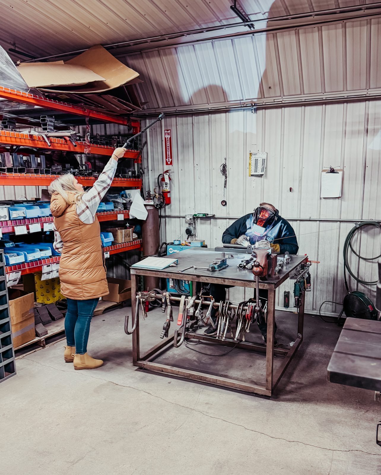Samantha filming in a fabrication shop while a welder works