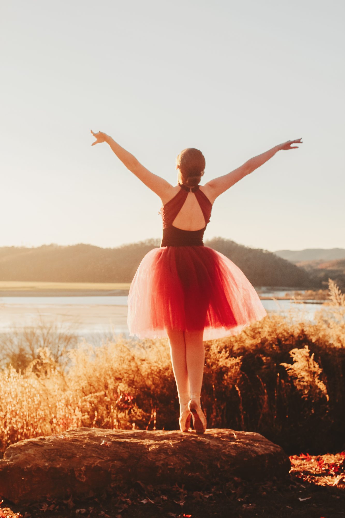 Dancer in deep rose tutu at golden hour, arms raised